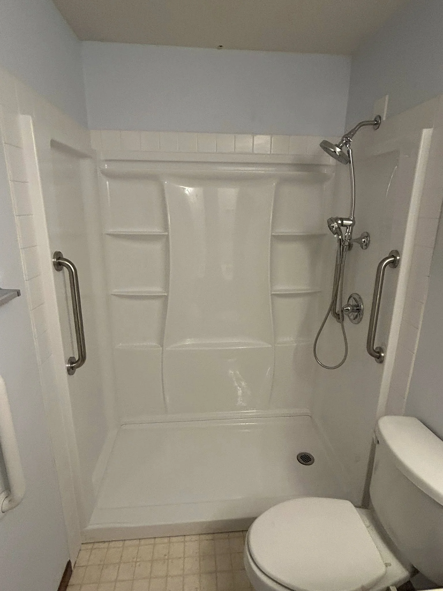 Newly installed shower stall with grab bars and chrome fixtures